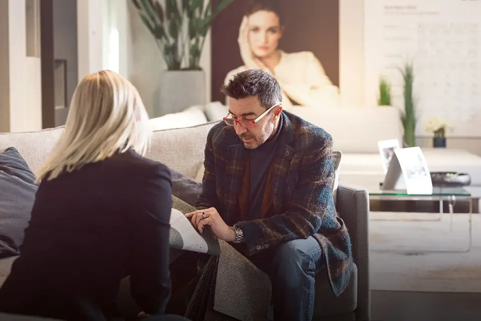 Neumaier Polsterberatung - Ein Berater von Neumaier erklärt einer Kundin verschiedene Stoffoptionen für Polstermöbel in einem gemütlichen Showroom, während sie zusammen über Stoffproben schauen.