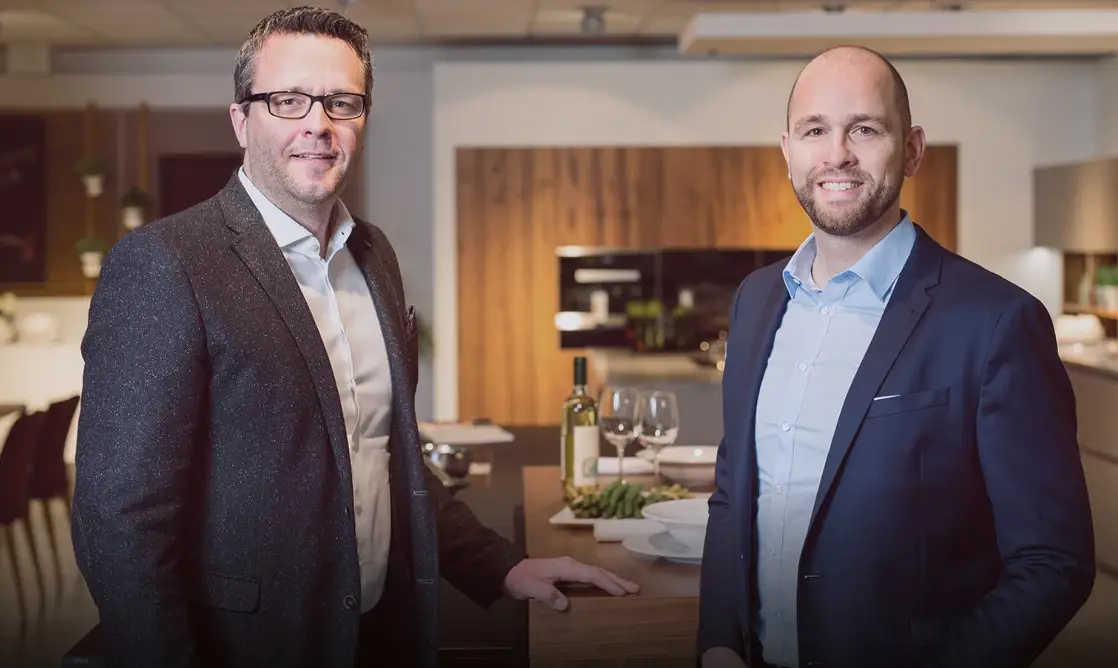Zwei Männer in Anzügen stehen in einer modernen Küche, die zu einem hochwertigen Küchenstudio gehört.
