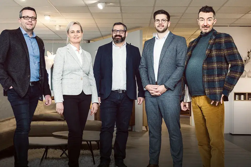 Das Verkaufsteam von Neumaier Einrichtungen posiert lächelnd für ein Gruppenfoto im Showroom. Fünf Teammitglieder sind in professioneller Kleidung zu sehen.